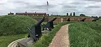 Cannons next to grassy embankment in front of brick fort above which the US flag is flying