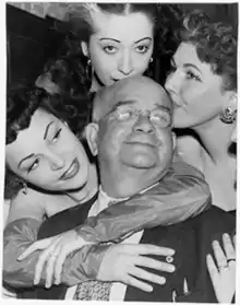 Black and white portrait of Francis Van Wie from 1952. This staged photograph was provided for press coverage following his 1952 arrest for bigamy (21 Aug 1952) and depicts the subject, characterized by the press as an unlikely Lothario due to his baldness, surrounded by three attractive women. One woman is hugging him from behind and her face is fully visible to his right. Two women are kissing the top of his head.