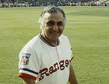 A man in a white baseball uniform with "Rangers" on the chest in red