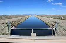 A picture of a canal from a low bridge over the canal. The canal flows straight off into the distance, and a mountain range rises above the horizon.