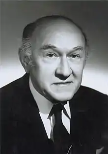 black-and-white picture of older white male wearing a dark suit, smiling at camera