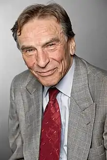 František Němec wearing a grey suit and red tie, smiling at camera