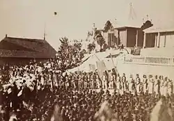 Crowds of civilians and soldiers observe a funeral in front of a tomb