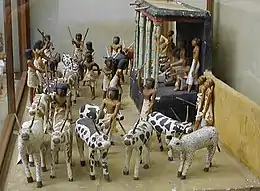 A string of various animals are led past a stage where several people count and record the animals as they pass.