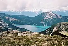 A symmetrical mountain rising above a turquoise-coloured lake in the foreground with glaciated mountains in the background