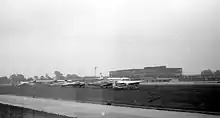 Small planes parked next to a runway, with terminal building in background