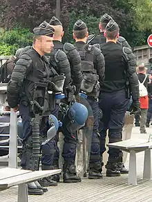 Riot control gear: body armour, shield, tear gas mask, apparatus for throwing tear gas canisters.