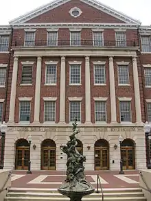 Front facade of a brick building with columns that has inscriptions above the entrance that read "School of Medicine" on the left and "School of Dentistry" on the right. In the foreground is a bronze statue.