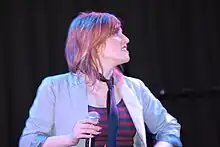 Geraldine Quinn on stage, holding a microphone and looking off to the side.