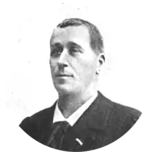 middle-aged white man, clean-shaven, with full head of neat dark hair; he is dressed in day clothes, with collar and tie