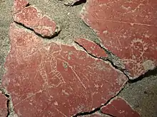 Bright red plaster plate on which a gladiator is drawn and appears in white.