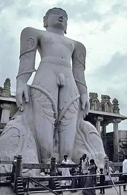 Giant grey stone statue of nude man with vines climbing legs to his arms