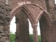 Part of a castle, with a huge semi-circular arch containing two smaller Norman arches dominating the picture. Through the arches, a ruined pillar can just be made out.