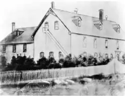 External view of school with students standing along white picket fence.