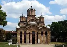 Exterior of the Gračanica monastery from the front, showing the tall and narrow central drum and dome and two of the four tall and narrow corner drums and domes of the square plan