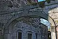 The arched head of a stone gateway has a carved keystone. Part of an old stone building is seen through the arch.