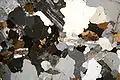 Granite in thin section under cross-polarized light in which feldspar crystals exhibit sericite alteration.