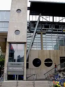 A photograph of the Emily Carr University of Art and Design's Granville Island campus, it is a large concrete building with circular windows on a narrow stone street