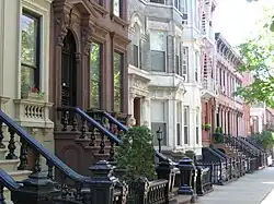 A view down a street with rowhouses in brown, white, and various shades of red