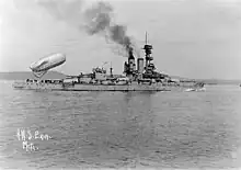 A large black and white ship in the center midground of the photo with a large balloon being launched from her stern