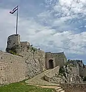 Stone tower with flag left from stone entrance.