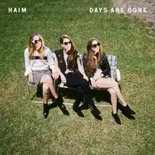 Three young women in sunglasses, sitting with legs crossed in lawn chairs in the grass.