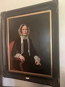 Colour oil painting of Hannah Napier Birks seated, wearing black dress with a white headdress and white ribbons, diamond brooch at base of bow tied around her neck