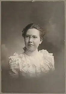 Young white woman in 1902, wearing a lacy high-necked white blouse and pince-nez eyeglasses.