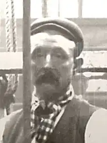 Man wearing working clothes being winched up in a galleried hall, while sitting on top of a sperm whale skeleton