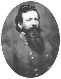 Blank and white photo shows a black-haired man with a heavy beard. He wears a gray military uniform with two rows of buttons.