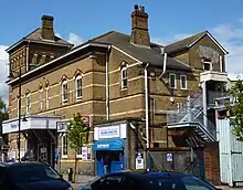 A brick building with decorative brickwork; a tower can be seen to the left and a stairway to the right. The main entrance is at the centre of the building; a taxi office is to the entrance's right.