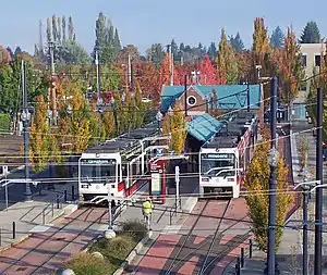 Photograph of a train station with two trains at its platforms with a road to the right