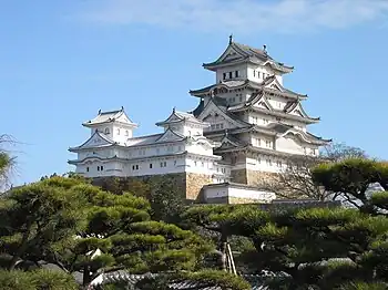 A white castle with one large five-storied tower and two smaller towers, all built on a stone base.