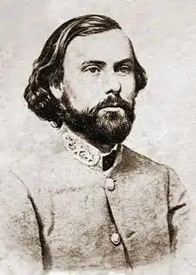 Black and white photo shows a dark-haired, bearded man in a gray military uniform with three stars on the collar.