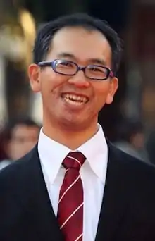 Portrait photo of a smiling Japanese man with glasses in a suit and tie