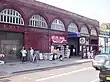 A red-bricked building with a sign reading "EXIT HOLLOWAY ROAD" in gold letters and a rectangular, blue sign reading "HOLLOWAY ROAD STATION"