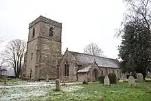 A stone church seen from the southwest, with a tower on the left, and a gabled south aisle and a porch on the right