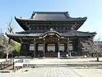 A large wooden building with an added pent roof enclosure and a Chinese style gable.