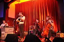 A color photograph of a four-person band performing on stage.