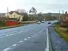 Large road w2ith houses to left and right and hills beyond.