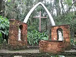 A stone altar with two images of Christian saints in a garden and on it a bow bearing a cross