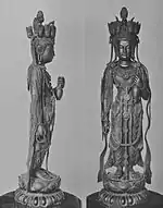 Front and profile view of a standing statue with her left arm bend forward. On the head there are small heads visible facing in various directions.