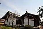 Wooden building with white walls and gabled roof next to a similar building.