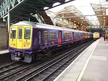 A commuter train at a station. Below the train, four rails are visible—two are for the wheels and one provides power. Above the train, a catenary power line is also visible.