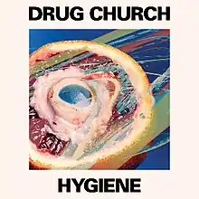 A beige square with a picture of an orange cut in half with a mitochondria model within the orange. Above the image reads "DRUG CHURCH" in black, all capital letters. Beneath the image reads "HYGIENE" in black, all capital letters.