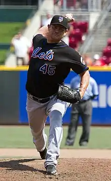 A man in a black baseball jersey and cap and gray pants