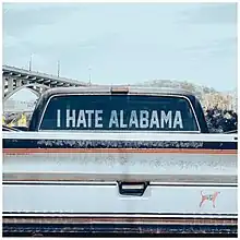 The official cover for "I Hate Alabama", featuring a white pickup truck with the words "I Hate Alabama" printed on its back windshield. On the truck's bumper, a sticker is shown, showing a dog with the official state flag of Tennessee.