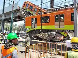 One of the railcars is being lifted by a crane. Behind it, the second railcar still hanging. Below them, a car is seen below the debris.