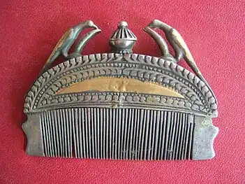 Indian metal comb for keeping hair in place, adorned with a pair of birds. After removing the central stopper, perfume can be poured into the opening in order to moisten the teeth of the comb and the hair of the wearer.