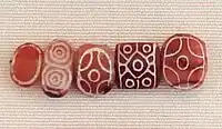 Indian carnelian beads with white design, etched in white with an acid, imported to Susa in 2600–1700 BCE. Found in the tell of the Susa acropolis. Louvre Museum, reference Sb 17751. These beads are identical with beads found in the Indus Civilization site of Dholavira.